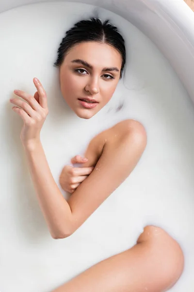 Vue de dessus de jolie femme se détendre dans le bain avec du lait et en regardant la caméra — Photo de stock