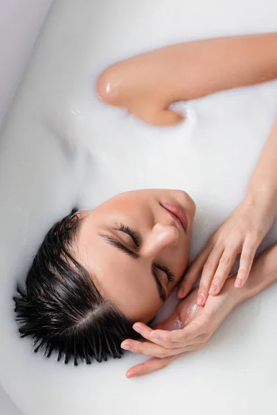 Vista aérea de la sensual mujer cogida de la mano cerca de la cara mientras toma un baño de leche - foto de stock