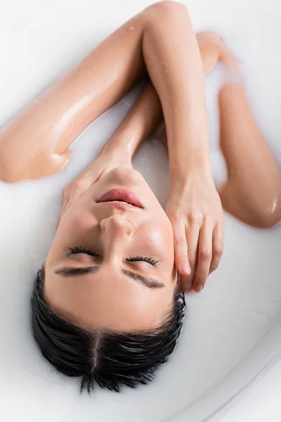 Overhead view of pretty woman touching face while relaxing in milk bath — Stock Photo