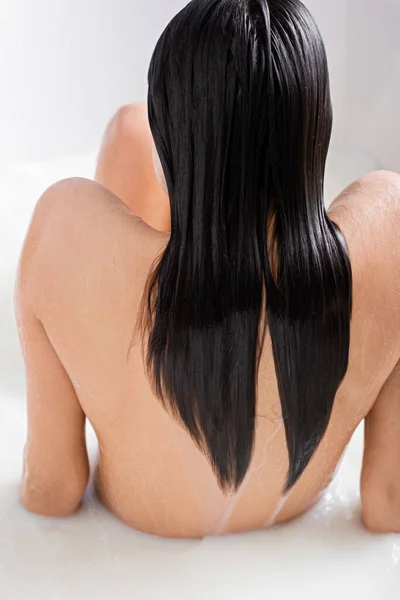 Vista posterior de mujer joven con el pelo mojado sentado en la bañera con leche - foto de stock