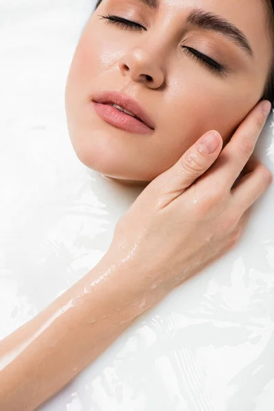 Pretty young woman touching face while relaxing in bath with milk — Stock Photo