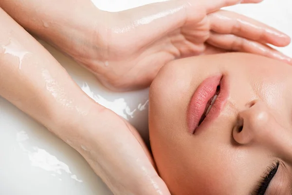 Partial view of young woman touching face while bathing in milk — Stock Photo