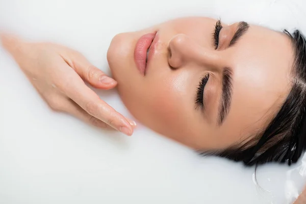 Giovane donna che si tiene per mano vicino al viso mentre si fa il bagno nel latte — Foto stock