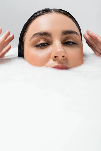 Junge Frau blickt in die Kamera, während sie in ein Bad mit Milch eintaucht — Stockfoto