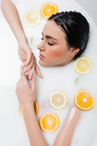 Вид женщины, принимающей молочную ванну с ломтиками лимона и апельсина — стоковое фото