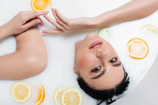 Sensual woman looking at camera while relaxing in milk bath with sliced citruses — Stock Photo