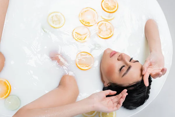 Vista aérea da mulher com os olhos fechados no banho leitoso com citrinos frescos — Fotografia de Stock