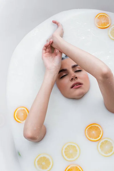 Junge Frau mit geschlossenen Augen genießt das Bad in Milch mit frischen Zitrusfrüchten — Stockfoto