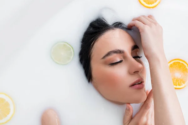 Overhead view of young woman with closed eyes taking milk bath with citrus slices — Stock Photo