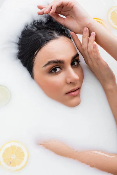 Sensual woman looking at camera while taking milk bath with citrus slices — Stock Photo