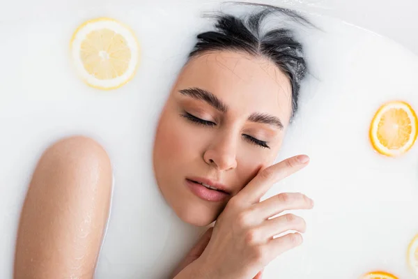 Top view of young woman enjoying bathing in milk with fresh, sliced citruses — Stock Photo