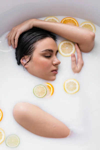 Junge Frau badet in Milch mit frischen, geschnittenen Zitrusfrüchten — Stockfoto