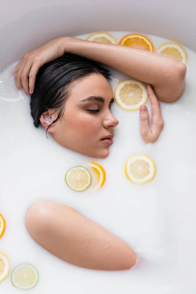 Mujer joven bañándose en leche con cítricos frescos en rodajas - foto de stock