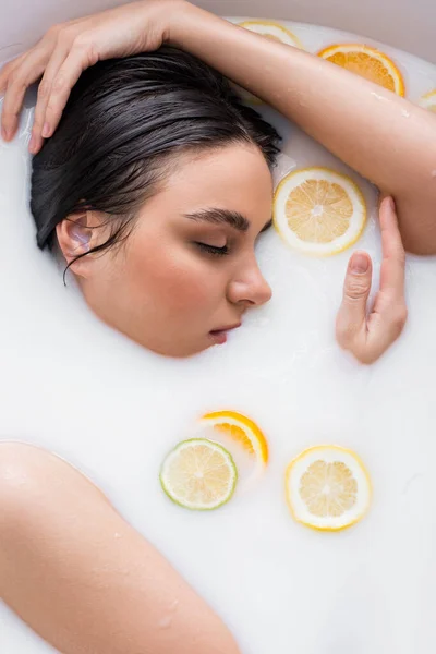 Молода жінка з закритими очима приймає молочну ванну з нарізаними цитрусовими фруктами — стокове фото