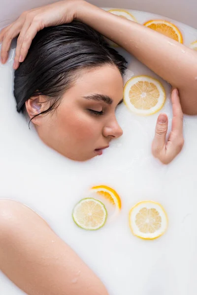 Mujer joven con los ojos cerrados tomando baño de leche con cítricos en rodajas - foto de stock