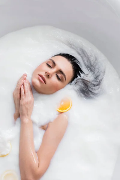Красивая молодая женщина купается в молоке с ломтиками лимона и апельсина — стоковое фото