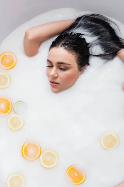 Hübsche Frau badet in Milch mit Scheiben frischer Zitrusfrüchte — Stockfoto