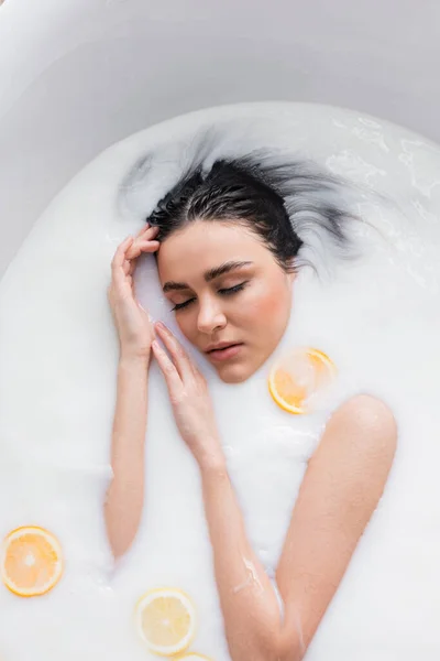 Вид на красивую женщину купающуюся в молоке с апельсиновыми и лимонными ломтиками — стоковое фото