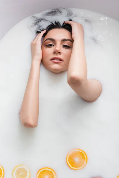 Hübsche Frau blickt in die Kamera, während sie sich im Milchbad mit Zitrusscheiben entspannt — Stockfoto