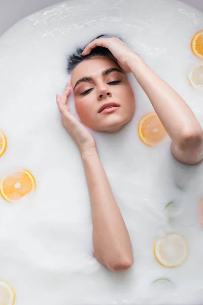 Draufsicht einer Frau mit geschlossenen Augen, die sich im milchigen Bad mit geschnittenen Zitrusfrüchten entspannt — Stockfoto