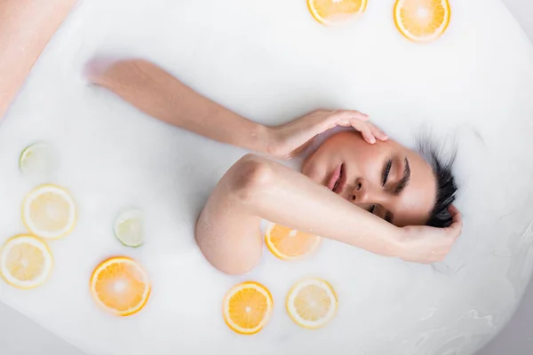 Vue du dessus de la jeune femme sensuelle se baignant dans le lait avec des agrumes tranchés — Photo de stock