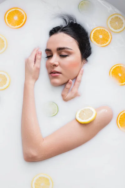 Jovem sensual mulher tomando banho de leite com frutas cítricas fatiadas — Fotografia de Stock