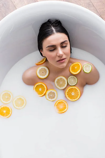 Vista aérea da jovem mulher em banho leitoso com fatias de citrinos frescos — Fotografia de Stock