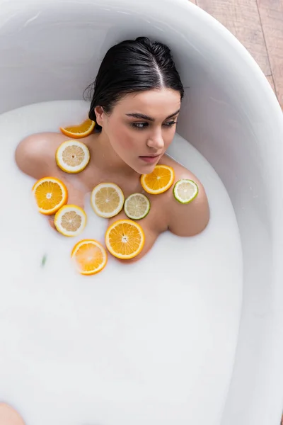 Young woman taking milk bath with sliced lemon, lime and orange — Stock Photo