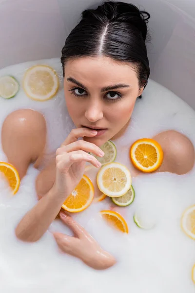 Mujer sensual mirando a la cámara mientras se baña en leche con cítricos en rodajas - foto de stock