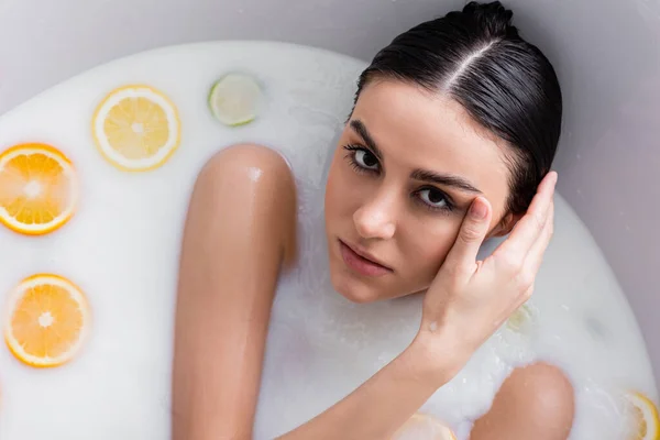 Pretty woman looking at camera while taking milk bath with citruses — Stock Photo