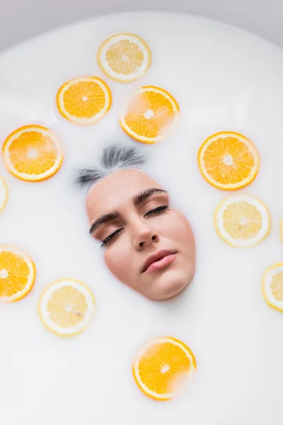 Femme aux yeux fermés prenant un bain laiteux avec des agrumes tranchés — Photo de stock