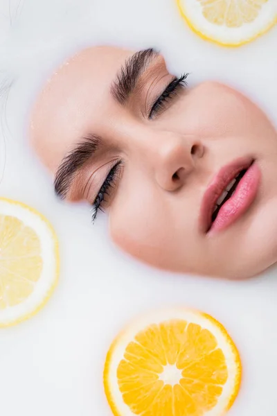 Vista de perto do rosto da mulher tomando banho no leite com limão fatiado e laranja — Fotografia de Stock