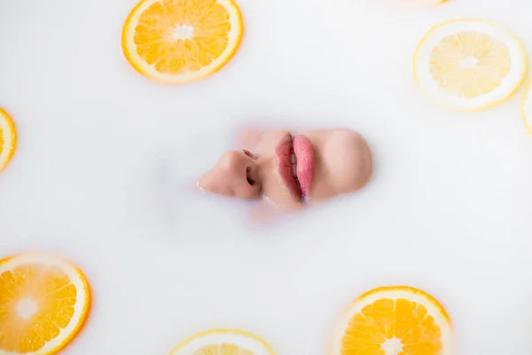 Vista superior de la cara femenina en baño de leche con rodajas de limón y naranja - foto de stock