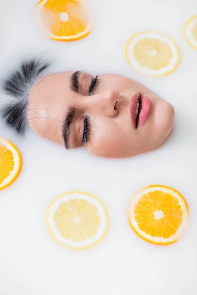 Hochwinkelaufnahme des Gesichts einer Frau, die in Milch mit Scheiben frischer Zitrusfrüchte badet — Stockfoto