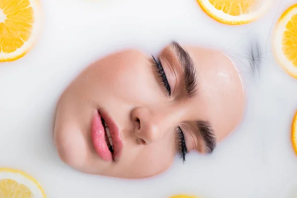 Close up view of female face with closed eyes in milk bath with citrus fruits — Stock Photo