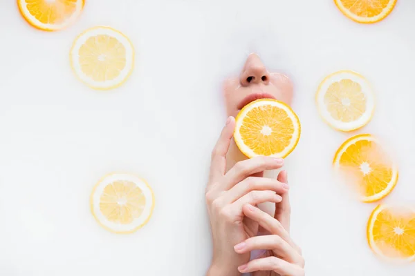 Вид зверху на жінку, що тримає апельсиновий шматочок під час занурення у молочну ванну — стокове фото