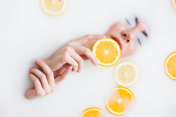 Vista superior de la mujer sosteniendo rebanada de naranja en baño de leche - foto de stock