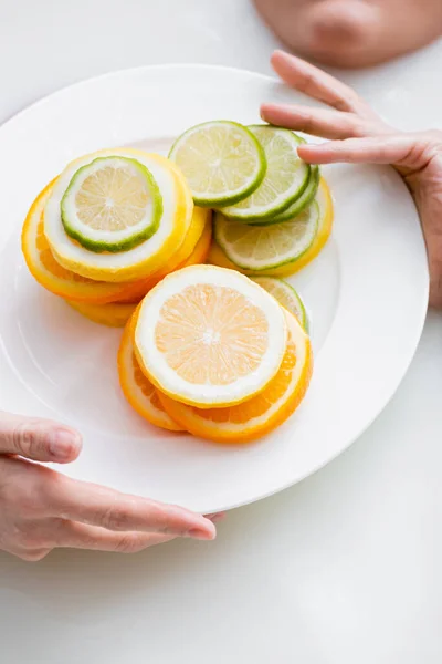 Cropped view of woman holding plate with sliced citruses while taking milk bath — Stock Photo