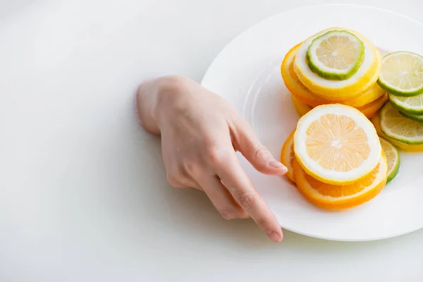 Partial view of female hand in milk bath near plate with sliced lemon, lime and orange — Stock Photo