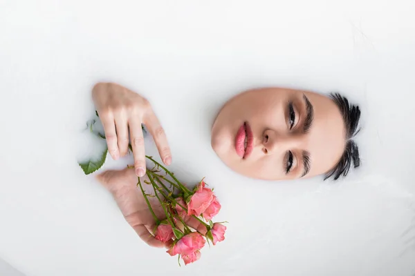 Mulher bonita olhando para a câmera enquanto toma banho de leite com rosas rosa — Fotografia de Stock