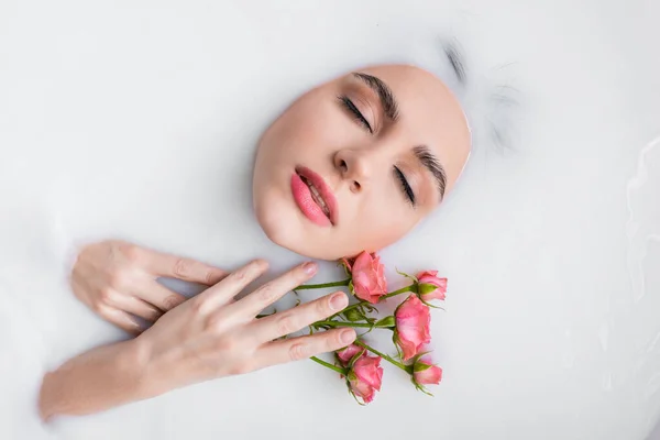 Vista superior de la mujer joven con rosas rosadas tomando baño lechoso - foto de stock