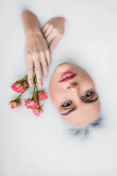 Вид зверху жінки, дивлячись на камеру під час купання в молоці з рожевими трояндами — стокове фото