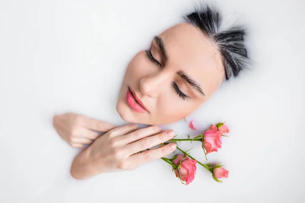 Junge Frau mit geschlossenen Augen und rosa Rosen, die in Milch badet — Stockfoto