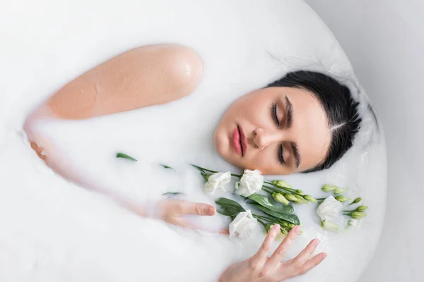 Pretty woman relaxing in milk bath with eustoma flowers — Stock Photo