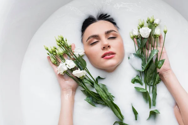 Jeune femme aux yeux fermés profitant de la baignade dans le lait avec des fleurs d'eustomie — Photo de stock