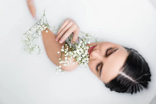 Draufsicht auf junge, sinnliche Frau, die Milchbad mit Zigeunerblumen genießt — Stockfoto