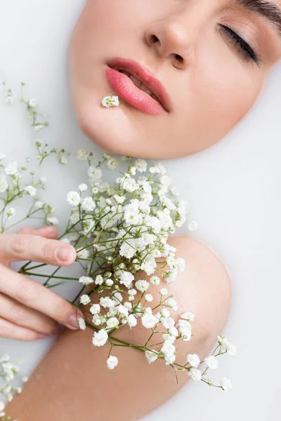 Vista recortada de la mujer joven en baño de leche con flores blancas, minúsculas - foto de stock