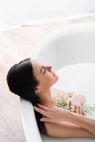 Junge Frau genießt Milchbad, während sie weiße, winzige Blumen in der Hand hält — Stockfoto