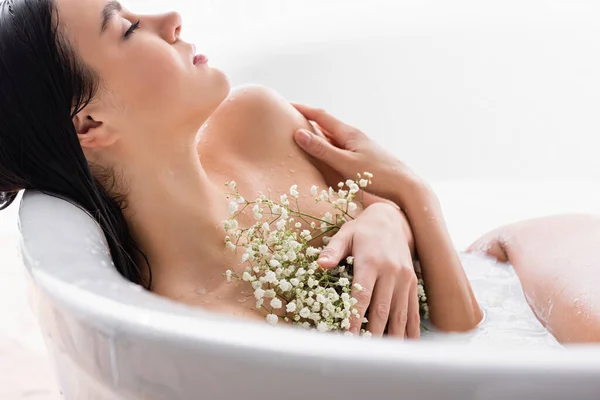 Jeune femme tenant des fleurs de gypsophila tout en prenant un bain de lait — Photo de stock