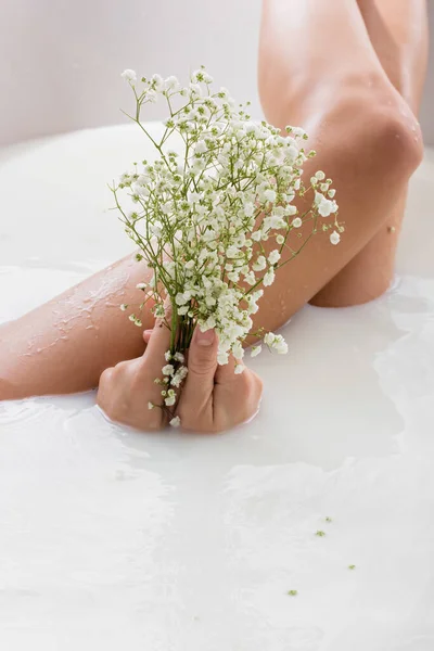 Partial view of woman holding white, tiny flowers while enjoying milk bath — Stock Photo